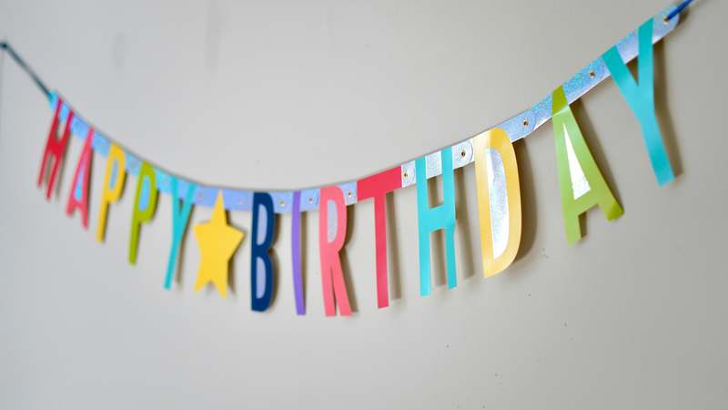 Bright pastel birthday banner, confetti-filled mason jars, and DIY paper garlands on a rustic wooden table